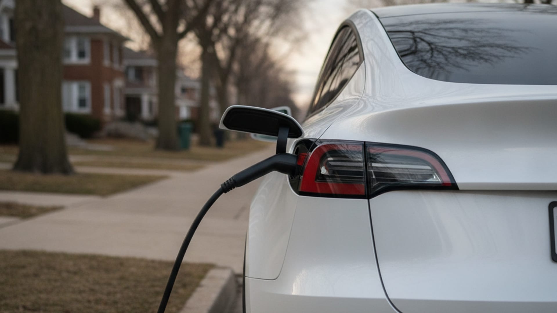 Charge Pro CHI technician in electric-blue polo connecting a NACS charging cable to a stranded Tesla Model Y on a Chicagoland street at golden hour